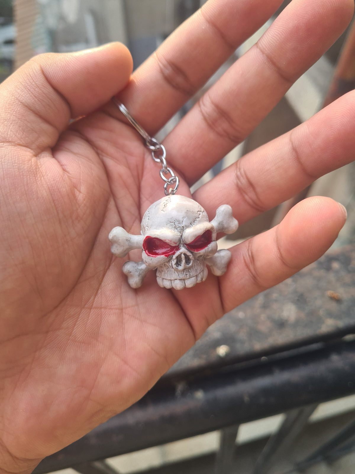 A skull and crossbones keychain with red eye sockets, held in a person's hand.